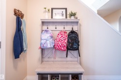 Built-in entryway bench with integrated storage and hooks, featuring a light wood-finish and visible staircase - 