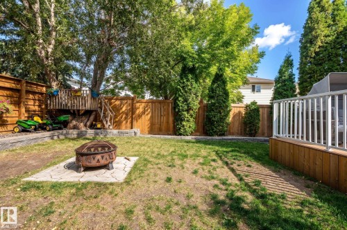 Private backyard featuring a wood privacy fence, a raised wood deck with white railings, and a fire pit on a paver base - 38 Dubonnet Way, St. Albert, AB 