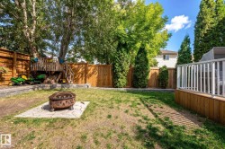 Private backyard featuring a wood privacy fence, a raised wood deck with white railings, and a fire pit on a paver base - 