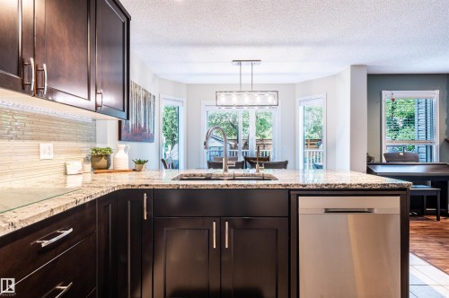 Kitchen featuring dark wood cabinetry, light granite countertops, a mosaic tile backsplash, and a stainless steel dishwasher - 38 Dubonnet Way, St. Albert, AB 