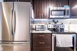 Stainless steel French door refrigerator, dark wood-finish cabinetry, stainless steel microwave, stone-finish countertops, and tile backsplash - 