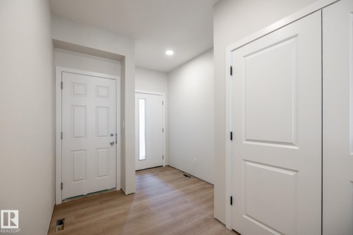 Entryway featuring wood-finish flooring, recessed lighting, white panel doors, and a front door with a full-length sidelight - 2358 Muckleplum Way Sw, Edmonton, AB 