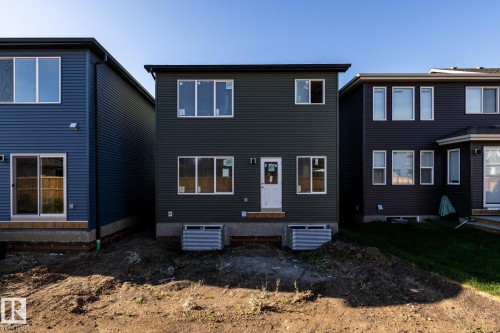 Rear elevation featuring dark green horizontal siding, multiple windows, and a white rear entry door - 2358 Muckleplum Way Sw, Edmonton, AB 