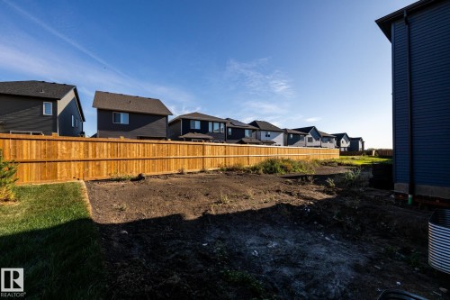 Expansive rear yard with a newly installed wood privacy fence, partially graded terrain, and a partially grassed area - 2358 Muckleplum Way Sw, Edmonton, AB 