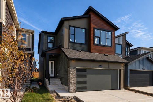 Contemporary exterior featuring mixed-material siding, a prominent wood-finish accent, and a modern garage door with integrated windows - 2358 Muckleplum Way Sw, Edmonton, AB 