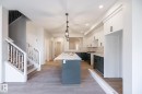 Spacious open-concept kitchen featuring a large central island, pendant lighting, two-tone cabinetry, and wood-finish flooring - 2358 Muckleplum Way Sw, Edmonton, AB 