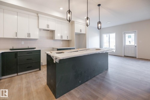 Contemporary kitchen featuring white upper cabinetry, dark lower cabinetry, a center island, wood-finish flooring, and pendant lighting - 2358 Muckleplum Way Sw, Edmonton, AB 