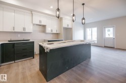 Contemporary kitchen featuring white upper cabinetry, dark lower cabinetry, a center island, wood-finish flooring, and pendant lighting - 