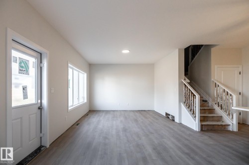Spacious interior featuring wood-finish flooring, white walls, and a staircase with white railings - 2358 Muckleplum Way Sw, Edmonton, AB 