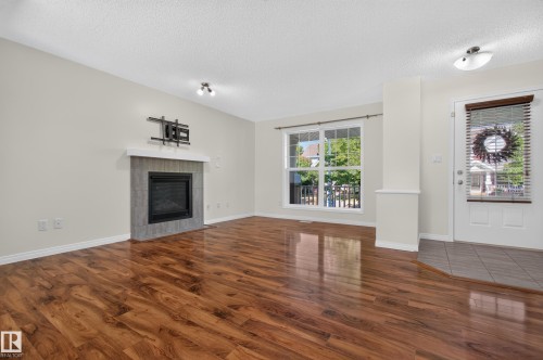 Wood-finish flooring throughout, tiled entry, and a fireplace with a light-colored mantel and gray-tiled surround - 6933 21A Avenue Sw, Edmonton, AB 