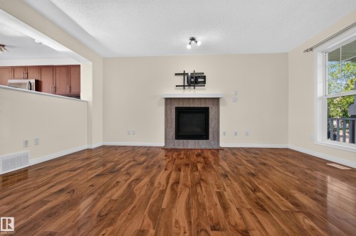 Wood-finish flooring, built-in fireplace with tile surround, white trim, and a large window - 6933 21A Avenue Sw, Edmonton, AB 