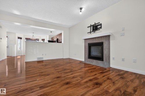 Wood-finish flooring, tiled fireplace with a mantel, and built-in ceiling lighting - 6933 21A Avenue Sw, Edmonton, AB 