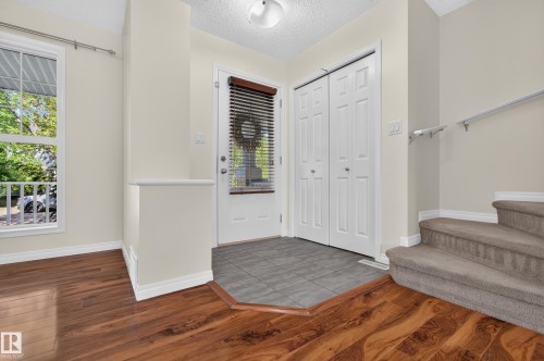 Entryway featuring wood-finish flooring, tiled landing, bi-fold closet doors, and staircase with carpeting - 6933 21A Avenue Sw, Edmonton, AB 