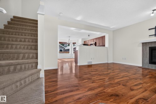 Expansive main living area featuring wood-finish flooring, a tiled fireplace with a mantel, and an open concept layout - 6933 21A Avenue Sw, Edmonton, AB 