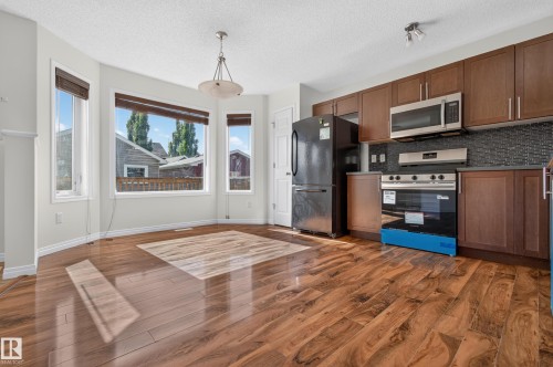 Wood-finish flooring throughout, bay windows, and a kitchen featuring a stainless steel microwave, black refrigerator, and a dark tile backsplash - 6933 21A Avenue Sw, Edmonton, AB 