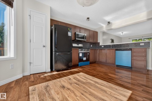 Kitchen featuring wood-finish flooring, wood cabinetry, dark countertops, and stainless steel appliances - 6933 21A Avenue Sw, Edmonton, AB 