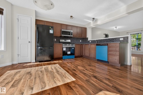 Kitchen featuring wood-finish flooring, dark wood cabinetry, a mosaic tile backsplash, and stainless steel appliances - 6933 21A Avenue Sw, Edmonton, AB 
