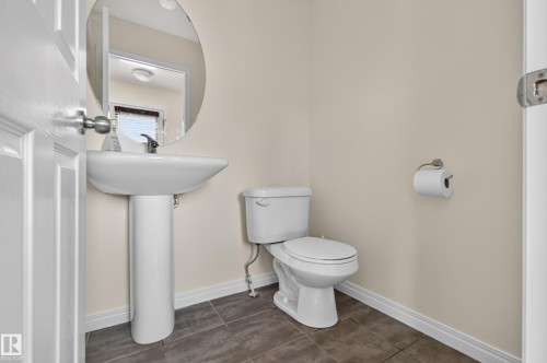 Pedestal sink with a wall-mounted mirror, ceramic tile flooring, and a toilet with a brushed nickel toilet paper holder - 6933 21A Avenue Sw, Edmonton, AB 