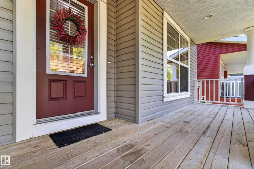 Covered front porch featuring wide plank wood flooring, grey horizontal siding, and a red entry door with upper window panes - 6933 21A Avenue Sw, Edmonton, AB 