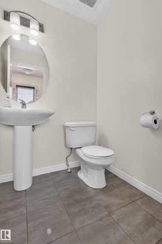 Pedestal sink, round mirror, white toilet, tile flooring, and overhead vanity lighting - 6933 21A Avenue Sw, Edmonton, AB 