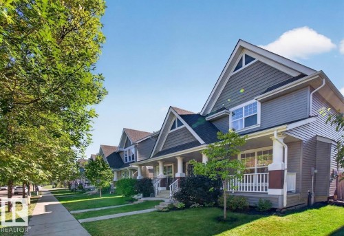 Exterior with shingle siding, covered front porch, gabled roofline, mature trees, and a manicured lawn - 6933 21A Avenue Sw, Edmonton, AB 