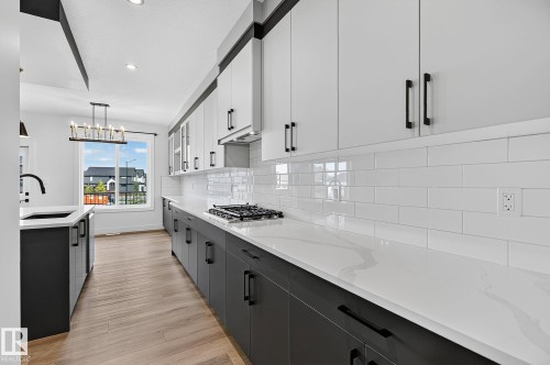 Kitchen featuring two-tone cabinetry, white subway tile backsplash, white countertops, wood-finish flooring, and a gas range - 22 Sydwyck Circle, Spruce Grove, AB 