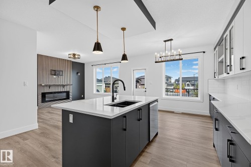 Modern kitchen island with a black sink and faucet, integrated dishwasher, and pendant lighting - 22 Sydwyck Circle, Spruce Grove, AB 
