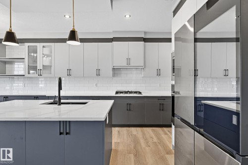 Two-tone cabinetry with contrasting upper and lower storage, white subway tile backsplash, light wood-finish flooring, and a stainless steel appliance suite - 22 Sydwyck Circle, Spruce Grove, AB 