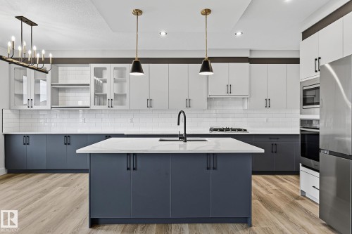 Kitchen featuring a large island with sink, two-tone cabinetry, stainless steel appliances, subway tile backsplash, and wood-finish flooring - 22 Sydwyck Circle, Spruce Grove, AB 