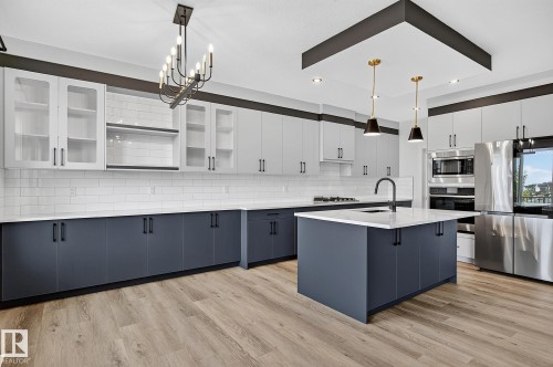 Modern kitchen featuring wood-finish flooring, a central island with a built-in sink, stainless steel appliances, white subway tile backsplash, and two-tone cabinetry - 22 Sydwyck Circle, Spruce Grove, AB 