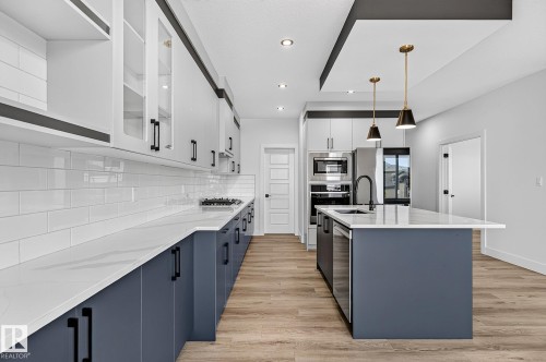 Gourmet kitchen featuring a central island, stainless steel appliances, wood-finish flooring, white subway tile backsplash, and two-tone cabinetry - 22 Sydwyck Circle, Spruce Grove, AB 