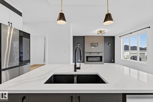 Expansive kitchen island with a dark composite sink and matte black faucet, illuminated by pendant lighting - 22 Sydwyck Circle, Spruce Grove, AB 