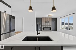 Expansive kitchen island with a dark composite sink and matte black faucet, illuminated by pendant lighting - 