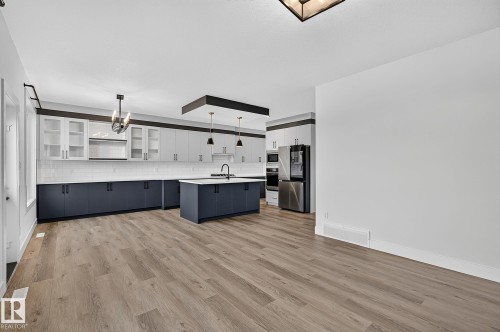 Wood-finish flooring, two-tone cabinetry, stainless steel appliances, white subway tile backsplash, and a kitchen island with pendant lighting - 22 Sydwyck Circle, Spruce Grove, AB 
