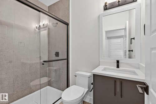 Frameless glass shower enclosure with a dark bronze frame, a single vanity with a white countertop, a rectangular undermount sink, and a dark bronze faucet - 22 Sydwyck Circle, Spruce Grove, AB 