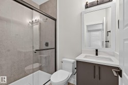 Frameless glass shower enclosure with a dark bronze frame, a single vanity with a white countertop, a rectangular undermount sink, and a dark bronze faucet - 