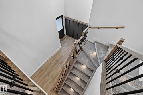 Multi-level staircase featuring carpeted treads with recessed lighting, wood-finish handrails, and black metal balusters - 22 Sydwyck Circle, Spruce Grove, AB 