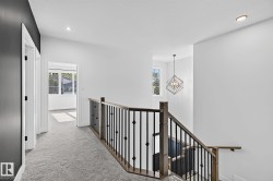 Carpeted hallway with white walls and dark accent wall, featuring a wood and iron baluster staircase - 