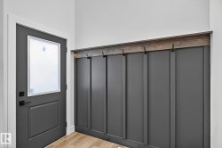 Entryway featuring a dark gray door with a frosted glass panel, matte black hardware, wood-finish flooring, and a built-in board and batten wall with a wood-finish top and integrated hooks - 
