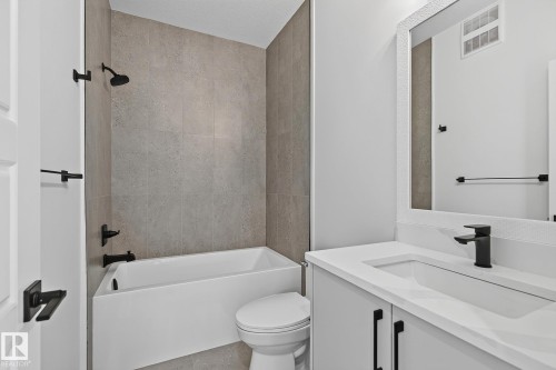 Bathtub with tile surround, matte black fixtures, white vanity with integrated sink, and framed mirror - 22 Sydwyck Circle, Spruce Grove, AB 