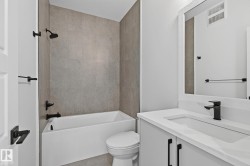 Bathtub with tile surround, matte black fixtures, white vanity with integrated sink, and framed mirror - 
