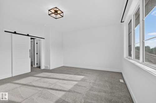 Recessed lighting, barn doors with black hardware, dark-frame ceiling light fixture, large window with black trim, and light gray carpet - 22 Sydwyck Circle, Spruce Grove, AB 
