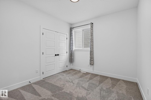 Neutral wall color, patterned carpeting, white window with horizontal blinds, and a double door with black hardware - 22 Sydwyck Circle, Spruce Grove, AB 