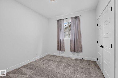 Neutral wall color, patterned carpet, window with white trim, and white paneled closet doors with black hardware - 22 Sydwyck Circle, Spruce Grove, AB 