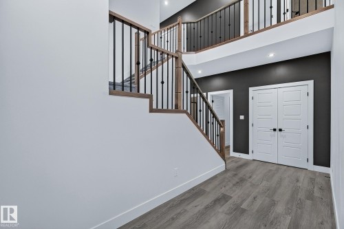 Two-story entry with wood-finish flooring, a dark accent wall, and a staircase featuring wood handrails and black metal balusters - 22 Sydwyck Circle, Spruce Grove, AB 