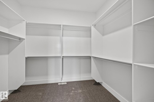 Walk-in closet with extensive built-in shelving, multiple hanging rods, and dark carpet flooring - 22 Sydwyck Circle, Spruce Grove, AB 