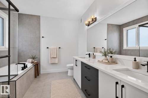 Dual vanity with undermount sinks and white countertops, matte black hardware, integrated bathtub with a glass enclosure, and large format tile flooring - 22 Sydwyck Circle, Spruce Grove, AB 