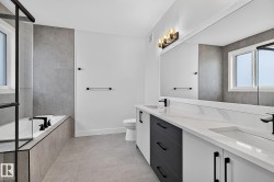 Spacious bathroom featuring a dual vanity with white countertops, integrated sinks, and black fixtures - 