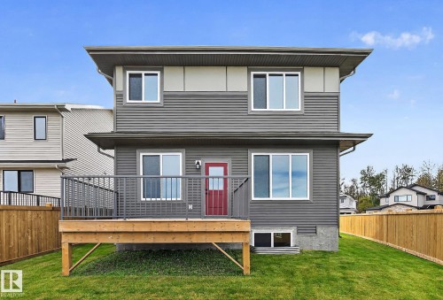 Two-story exterior with horizontal siding, a wood-finish deck with metal railings, a vibrant red entry door, and a manicured lawn - 22 Sydwyck Circle, Spruce Grove, AB 