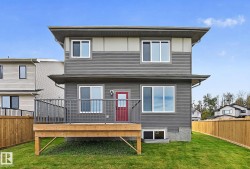 Two-story exterior with horizontal siding, a wood-finish deck with metal railings, a vibrant red entry door, and a manicured lawn - 